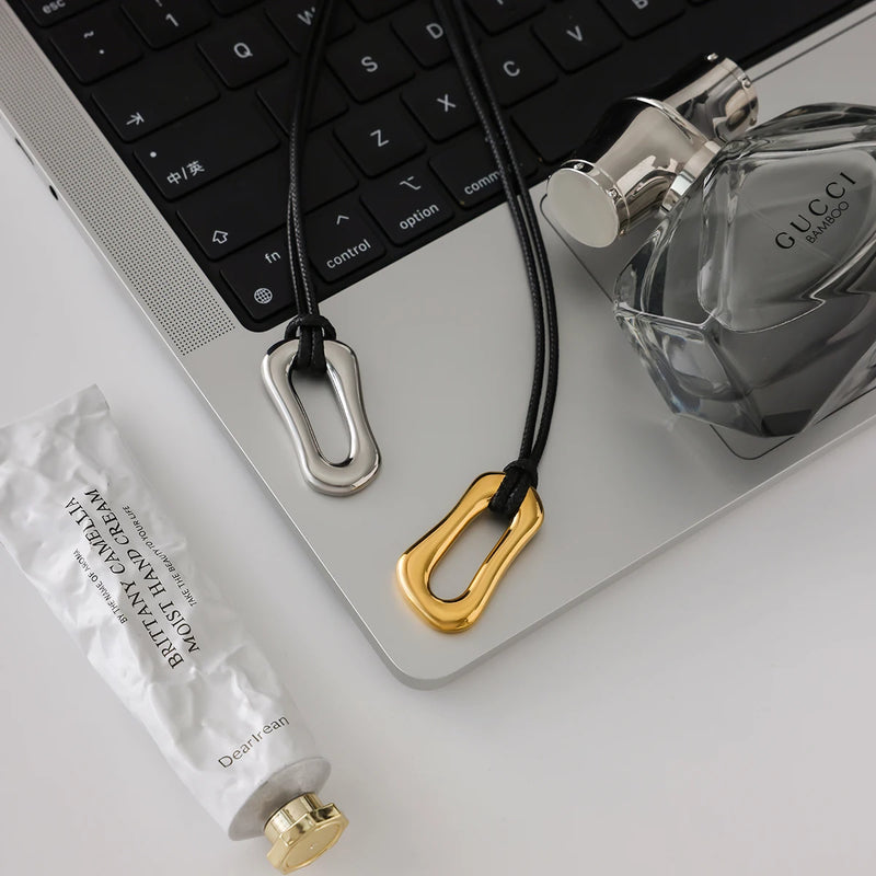 Cord necklaces with link pendants on a laptop beside a perfume