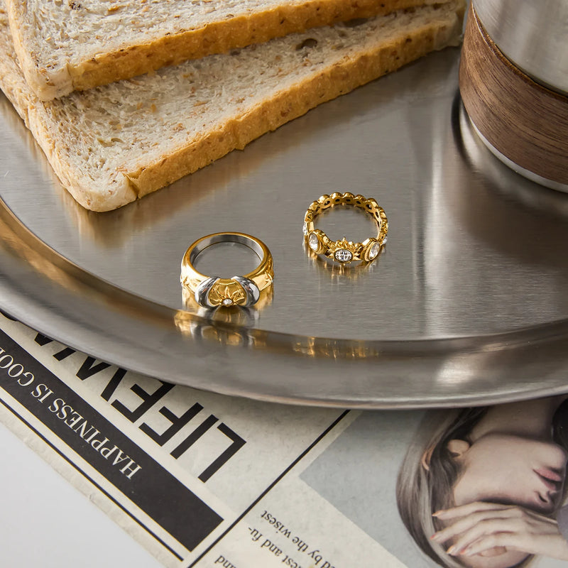 Two crystal-set rings on a metal tray beside toast and a cup