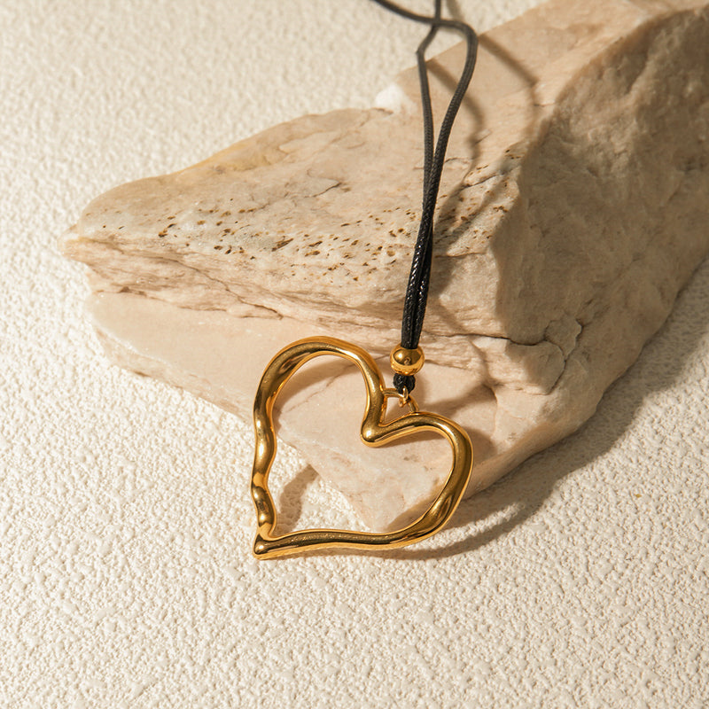 Open heart cord necklace resting against pale stone on sand