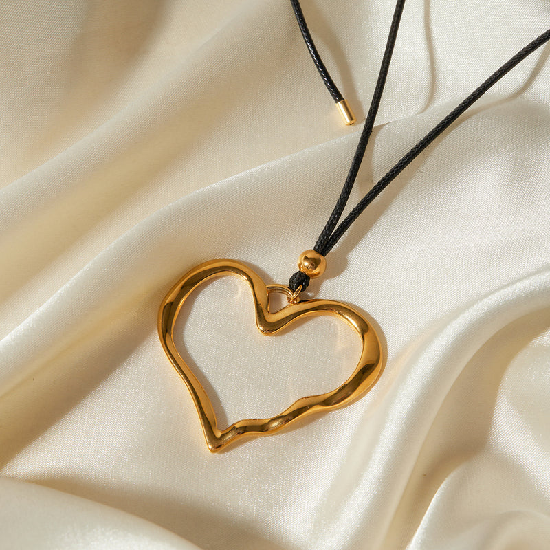 Gold-tone open heart pendant on a cord over cream satin