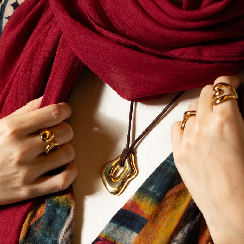 Gold-tone sculptural pendant on a cord against a red scarf