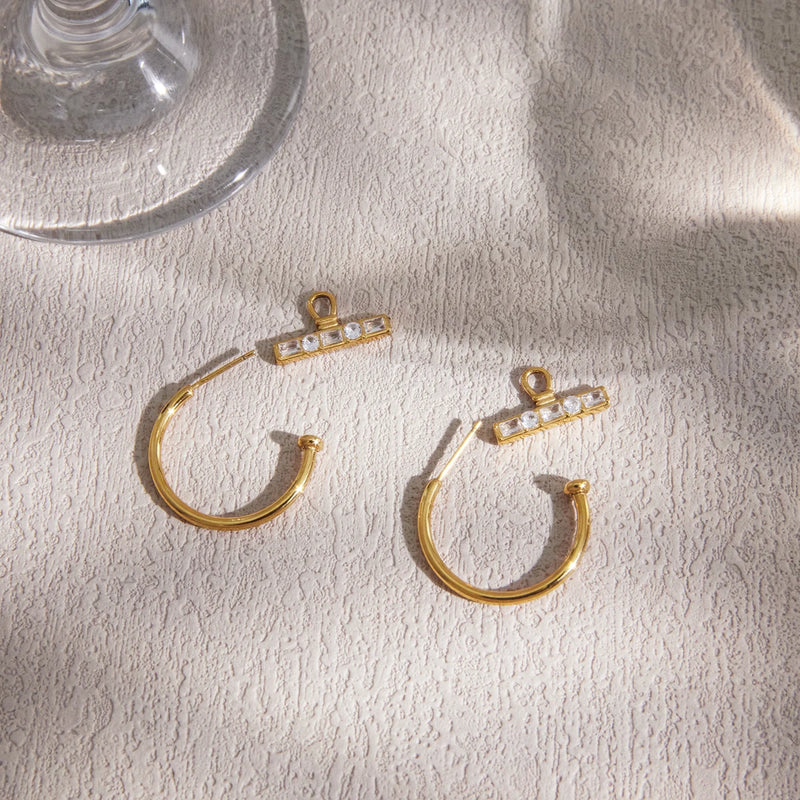 Pair of C-shaped hoops with crystal T-bars on cream fabric