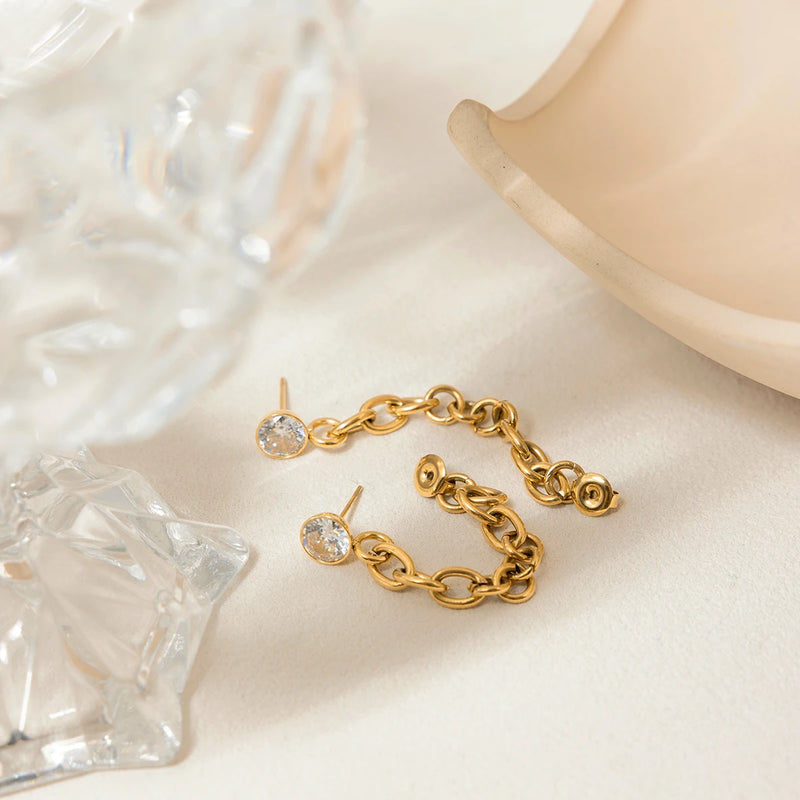 Chain drop stud earrings beside a clear glass form