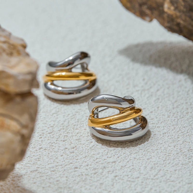 Pair of two-tone crossover hoops on a pale textured surface