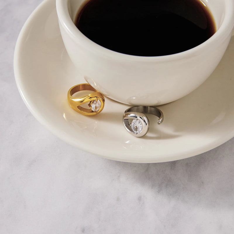Gold and silver-tone teardrop rings on a saucer beside a cup of coffee