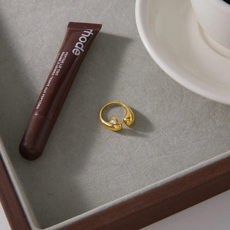 Heart stone open ring on a grey tray beside a lip product