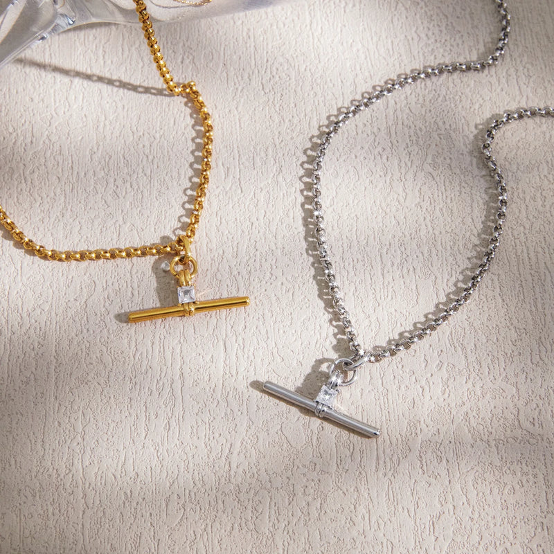 Gold-tone and silver-tone T-bar necklaces on a cream surface