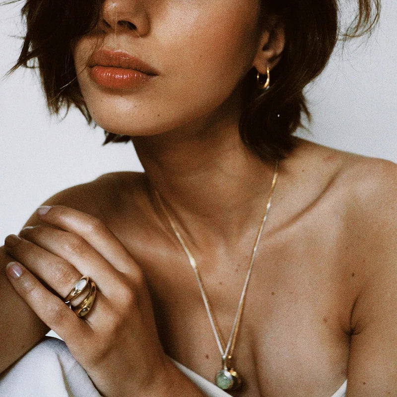 Domed ring worn on a hand with a pendant necklace visible