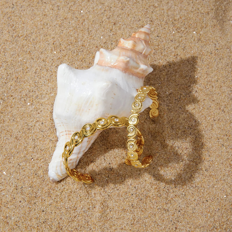 Spiral shell cuff propped against a conch shell on sand