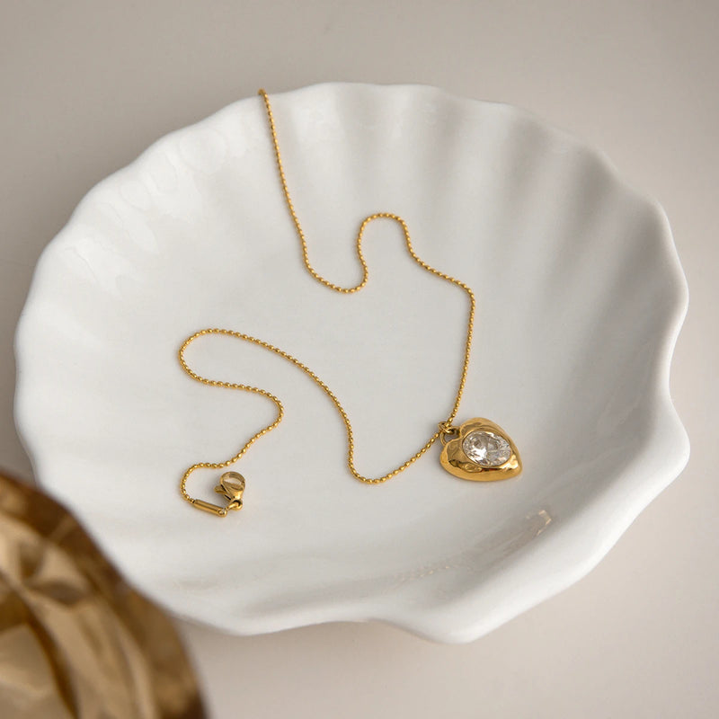 Cyrielle Crystal Heart Necklace coiled in a white shell dish