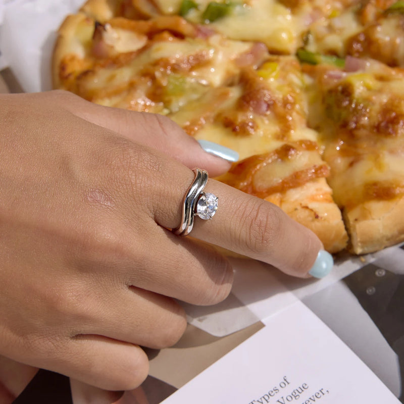 Wave rings worn on a hand reaching towards a pizza