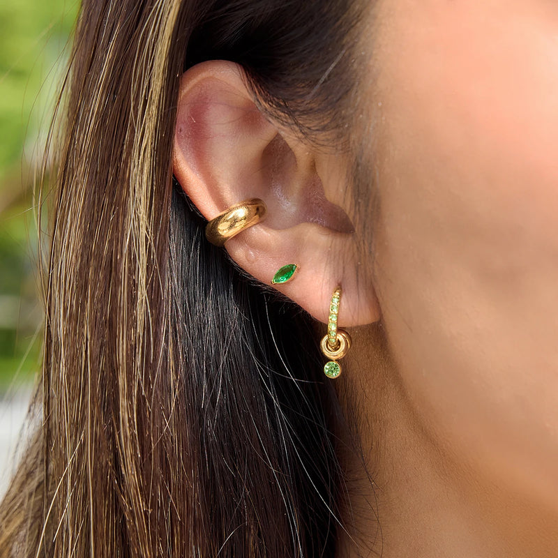 Small gold-tone hoops and a green stone stud worn in a stacked ear