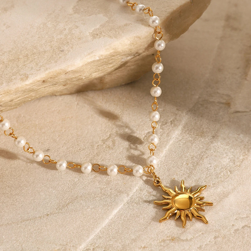 Pearl chain necklace with a gold-tone sun pendant, on pale stone