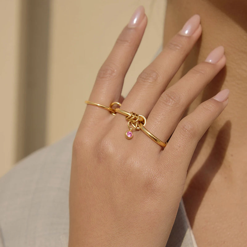 Slim band ring with a small pink stone charm worn on a finger