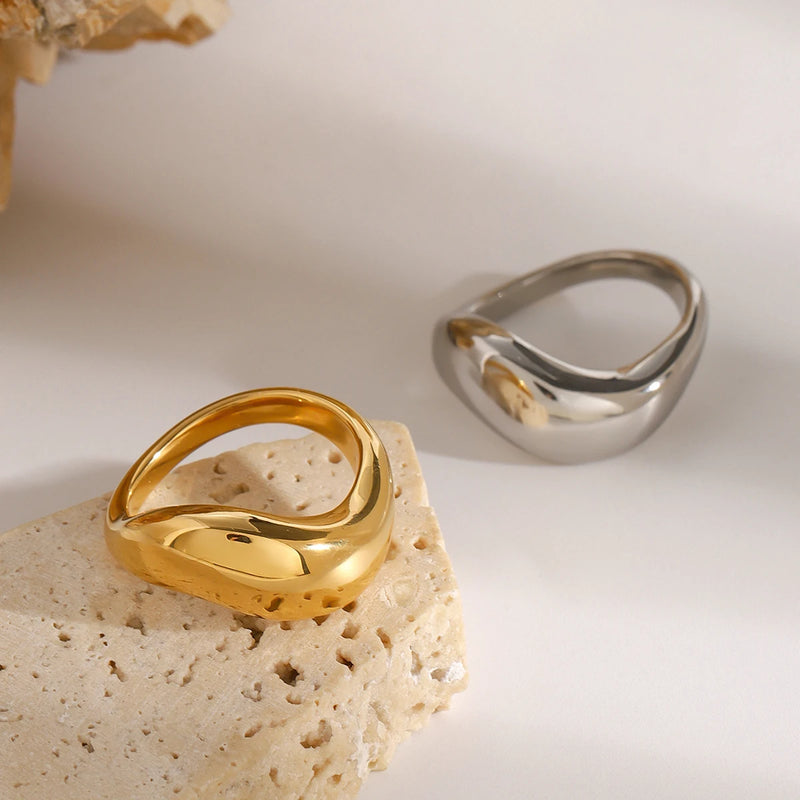 Ludivine Sculptural Wave Ring, both colourways resting on pale stone