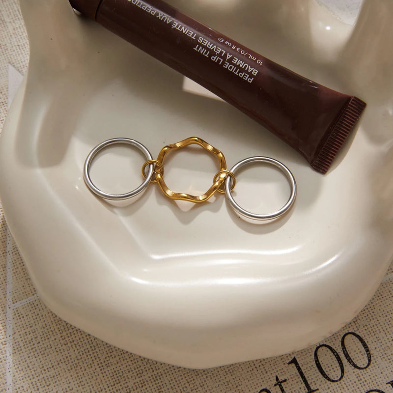 Gold-tone wave ring between two silver-tone bands on a dish