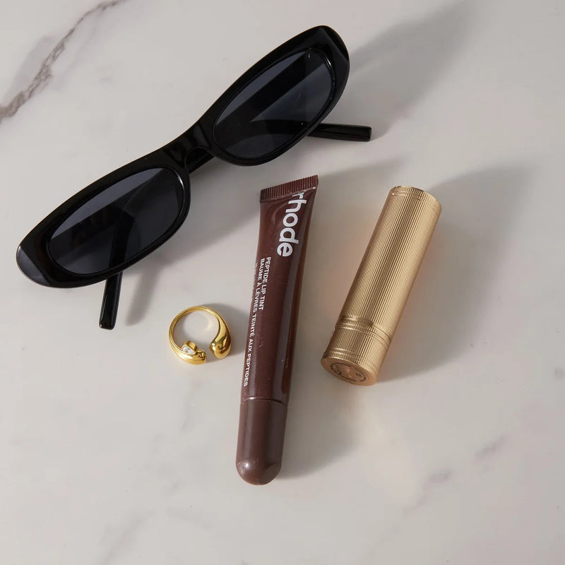 Open heart ring on a marble surface with sunglasses and cosmetics