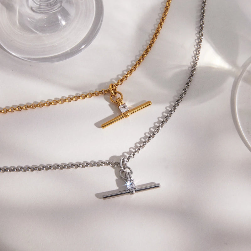 Two T-bar necklaces laid out beside a glass stem