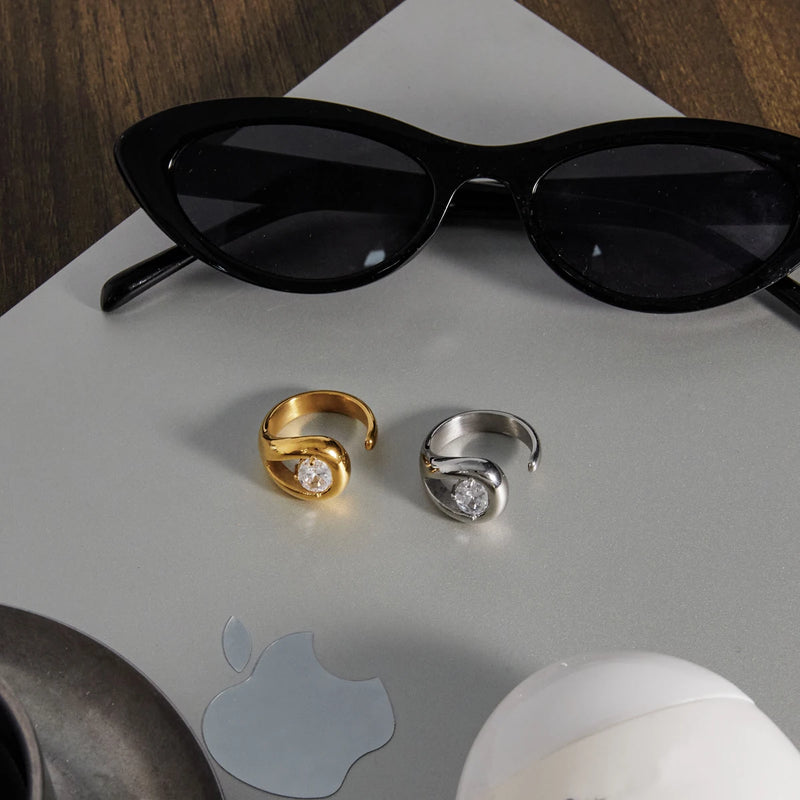 Both teardrop rings on a pale surface beside black sunglasses