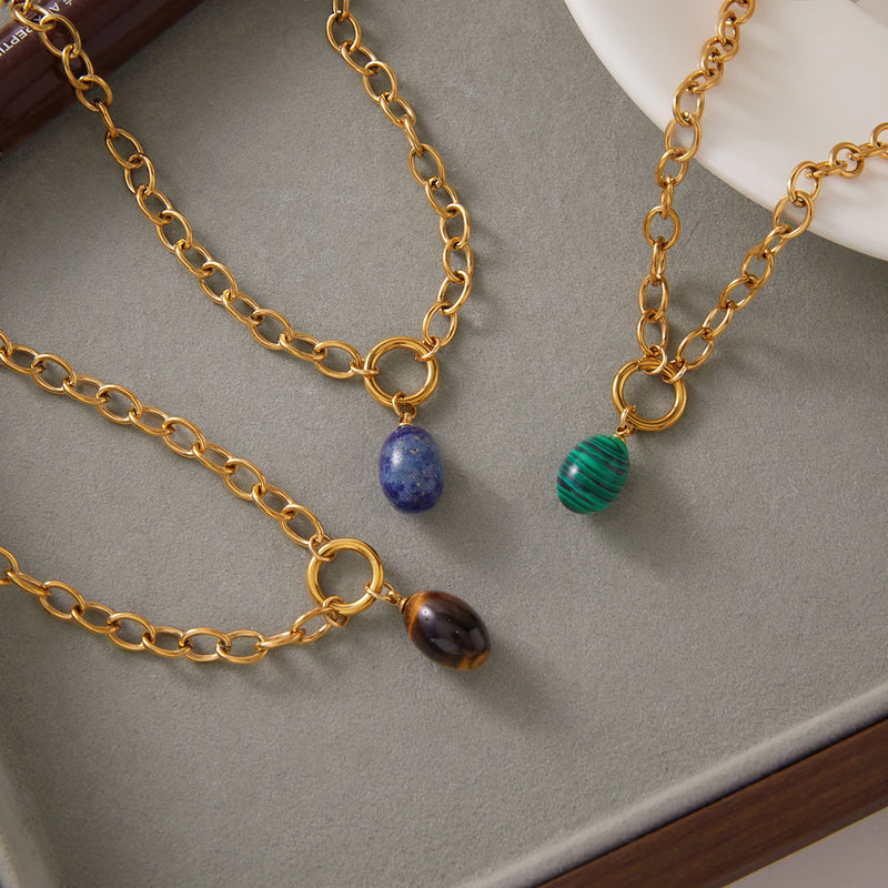 Two chain necklaces with blue and green stone drops on a grey tray