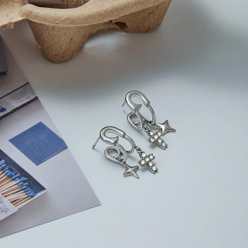 Two pairs of cross and star drop earrings on a pale surface