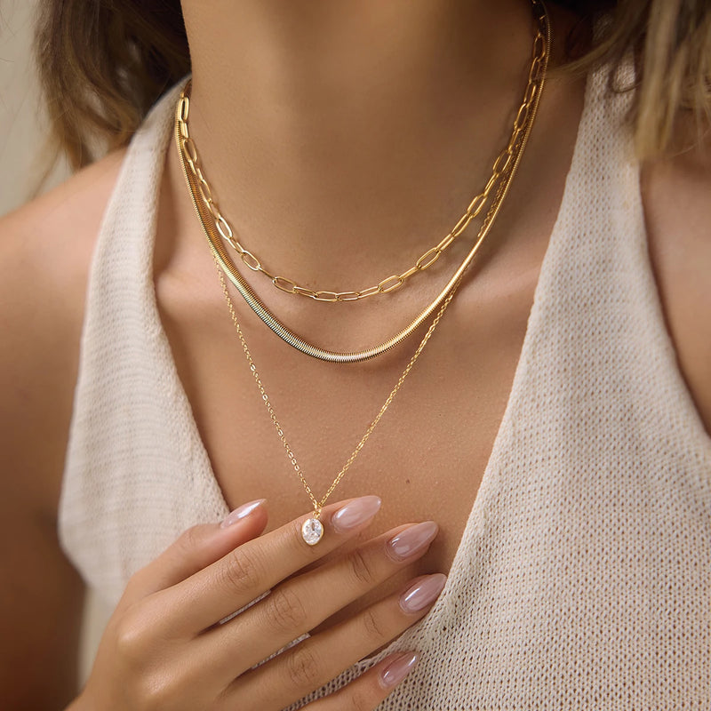 Triple-layer necklace worn, hand resting at the chest