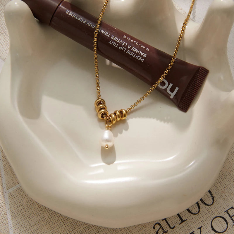 Necklace curled in a white dish beside a lip product