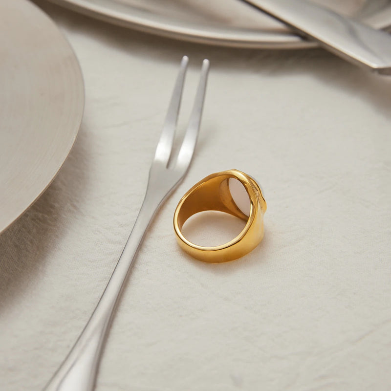 Gold-tone signet ring on a pale plate beside a fork