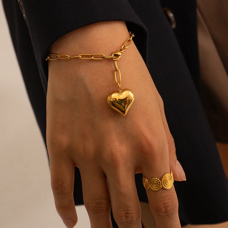 Heart charm bracelet worn on a wrist with two rings on the hand