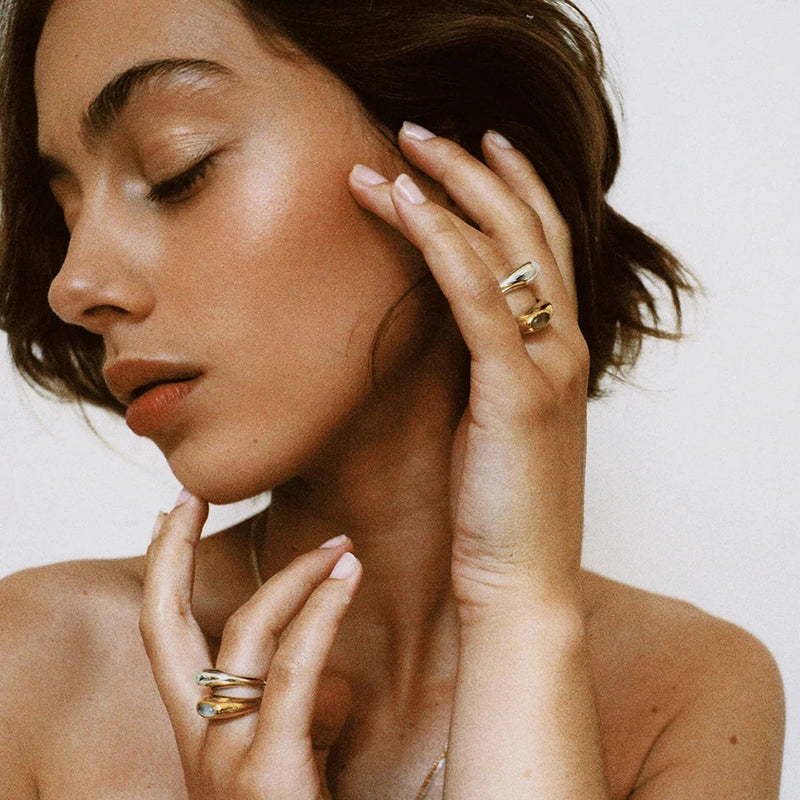 Domed cabochon rings worn on a hand raised to the face