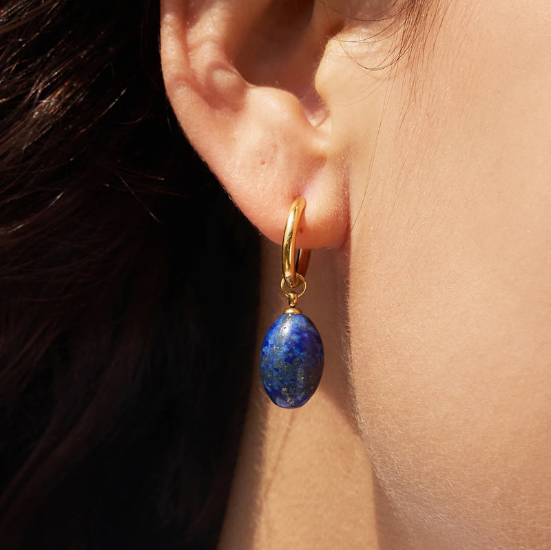 Close view of a blue stone drop hanging from a small gold-tone hoop