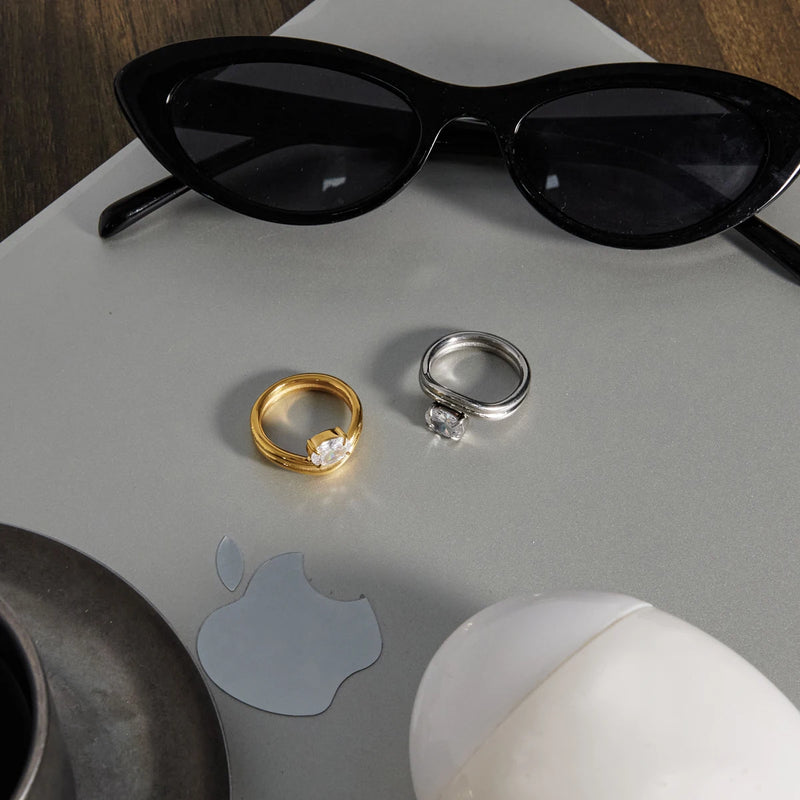 Gold and silver-tone wave rings on a pale surface with sunglasses
