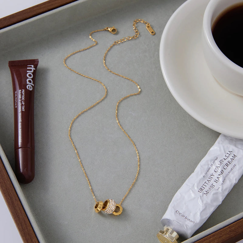 Crystal bead necklace on a grey tray beside a cup and lip product