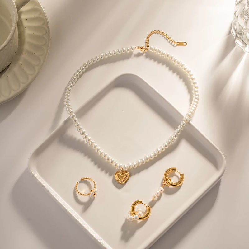 Pearl heart necklace laid out with two small hoop earrings