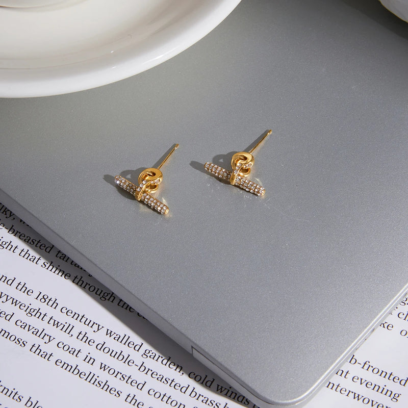 Two pave T-bar earrings on a grey surface over an open book