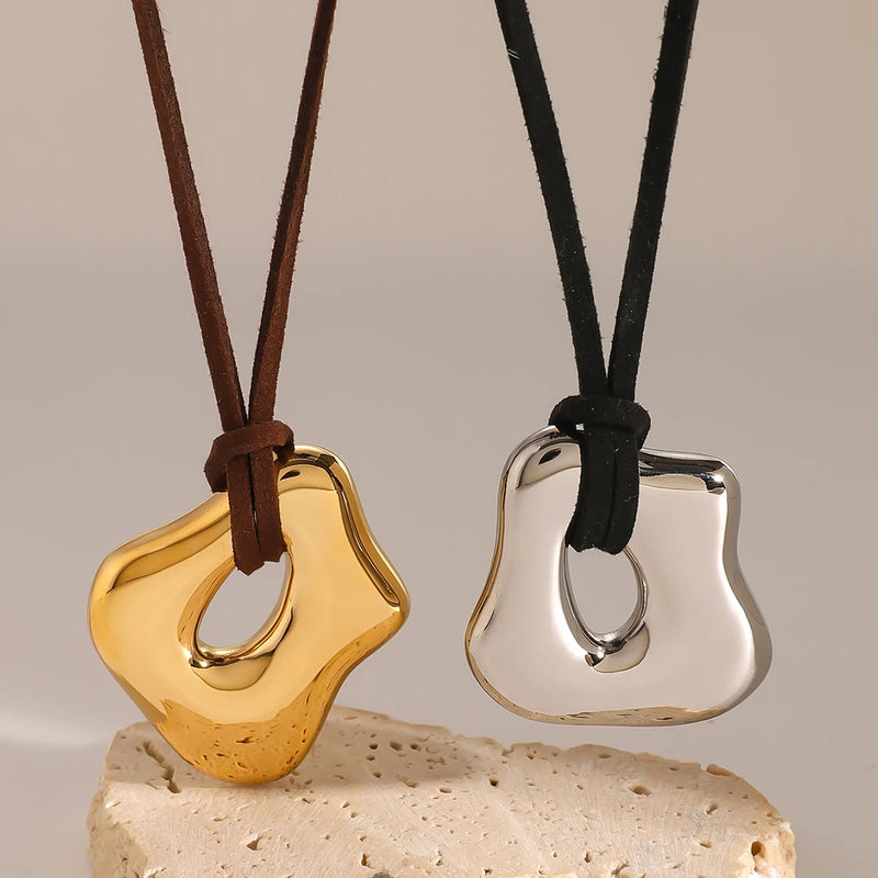 Two sculptural pendant cord necklaces standing on pale stone