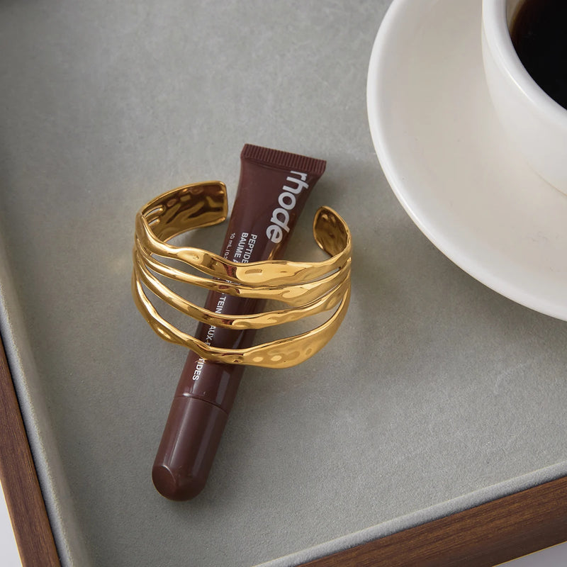 Molten wave cuff on a grey surface beside a lip product