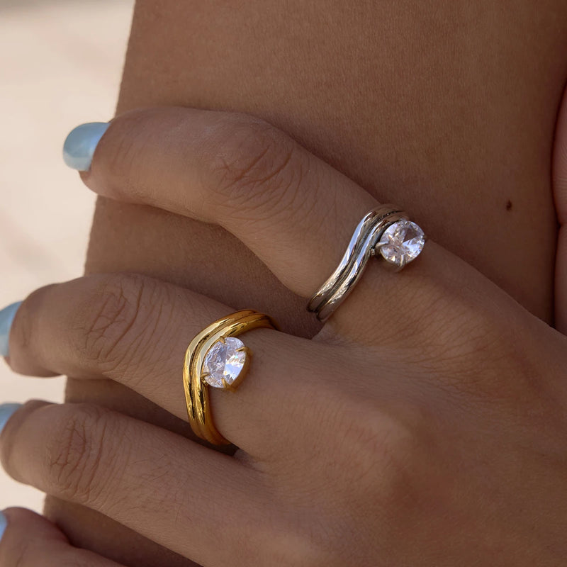 Gold-tone and silver-tone wave rings with clear stones, worn together