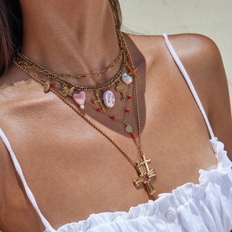 Layered chains with a cross pendant and pastel charms, worn