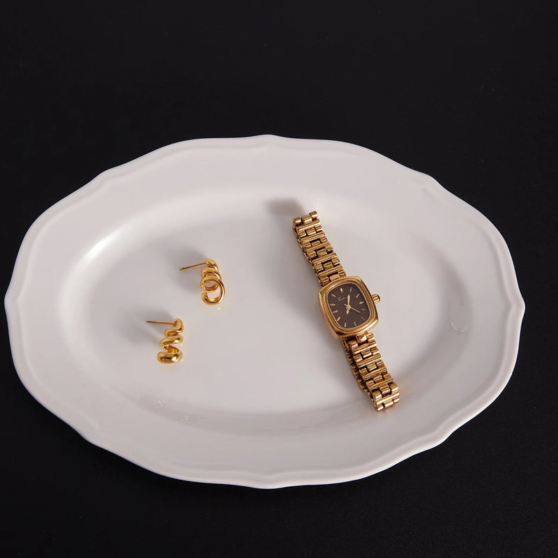 Spiral studs on a white plate beside a gold-tone watch
