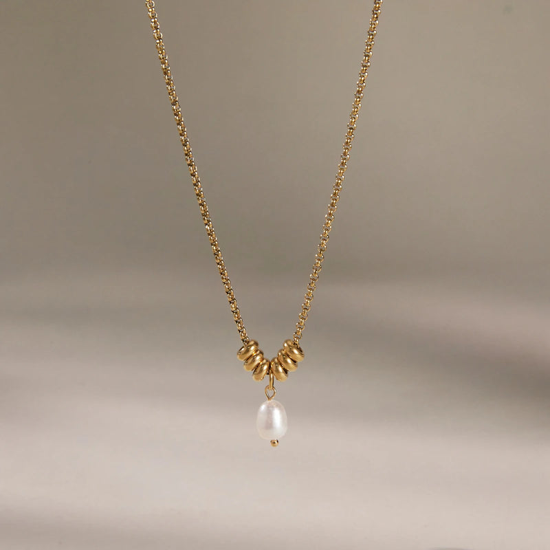 Fine beaded chain with a pearl drop against a plain background