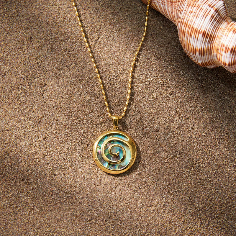 Shell pendant necklace on sand beside a striped seashell