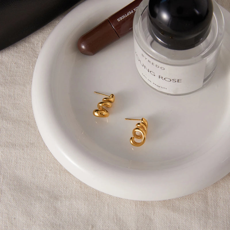 Pair of spiral studs on a white dish beside a perfume bottle