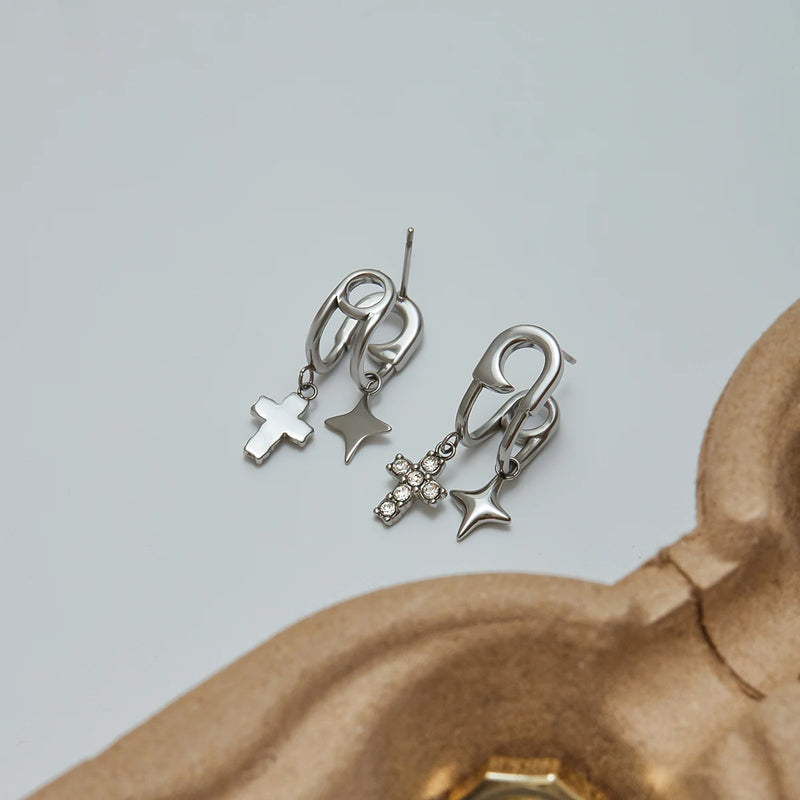 Silver-tone cross and star charm earrings on a pale background