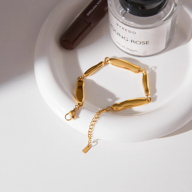 Pebble link bracelet on a white dish beside a perfume bottle