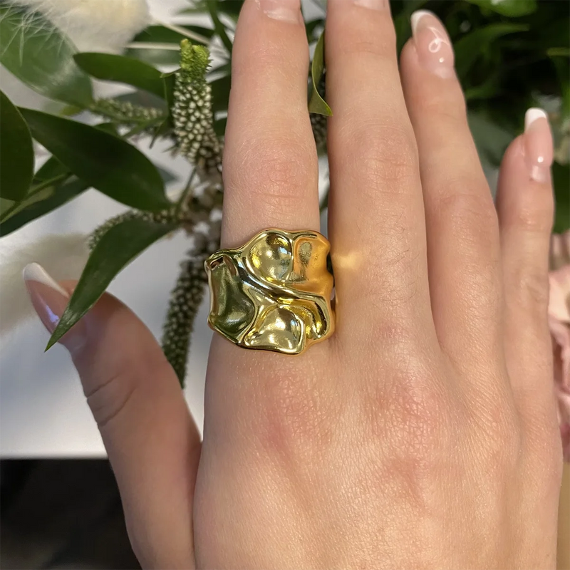 Wide gold-tone molten band ring worn on a finger