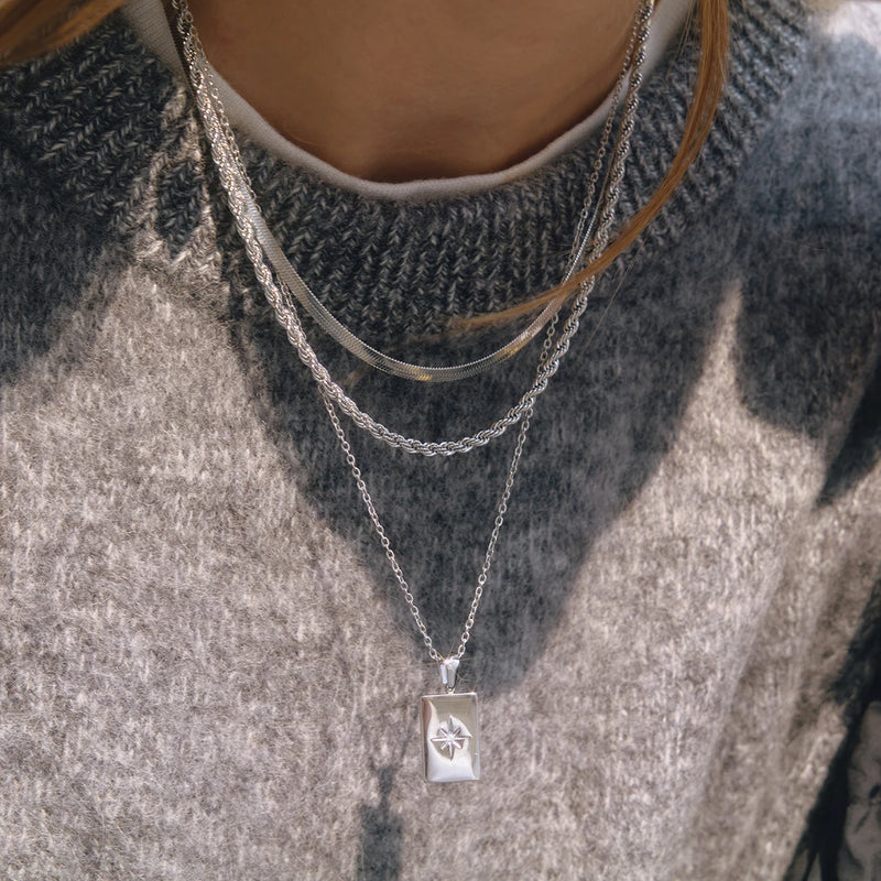 Three-strand silver-tone necklace with a star tag on a grey knit