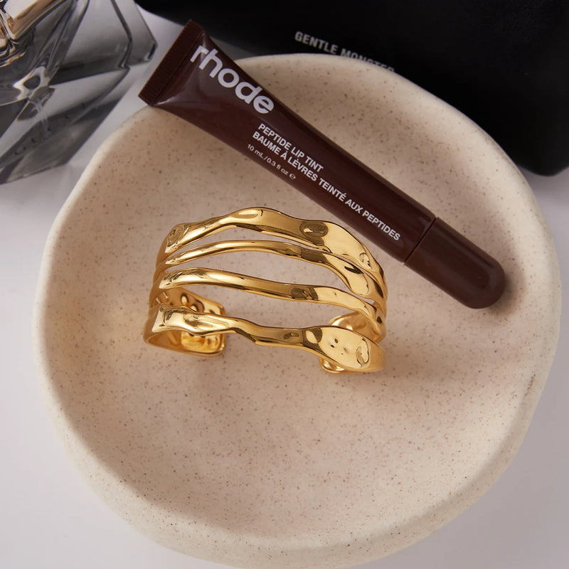 Open molten wave cuff in a pale dish beside a lip product