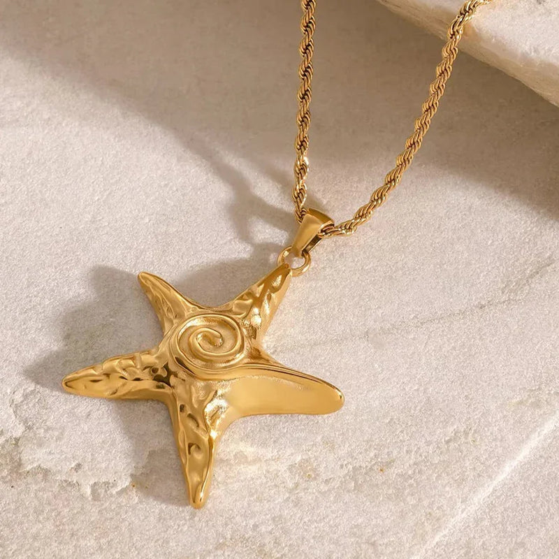 Gold-tone starfish pendant on a rope chain, resting on sand