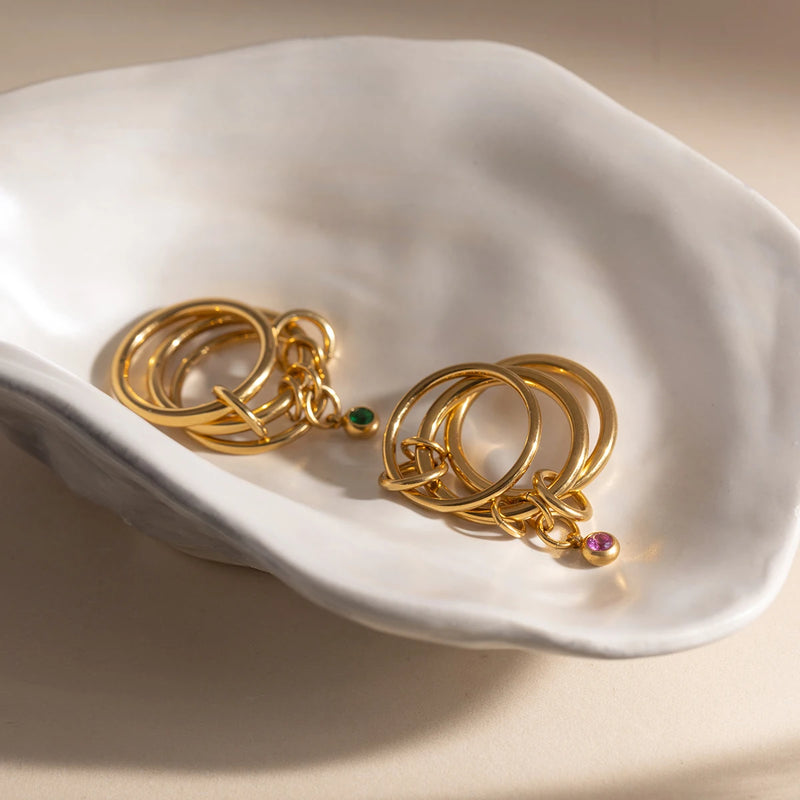 Linked charm rings with coloured stones on a white shell dish